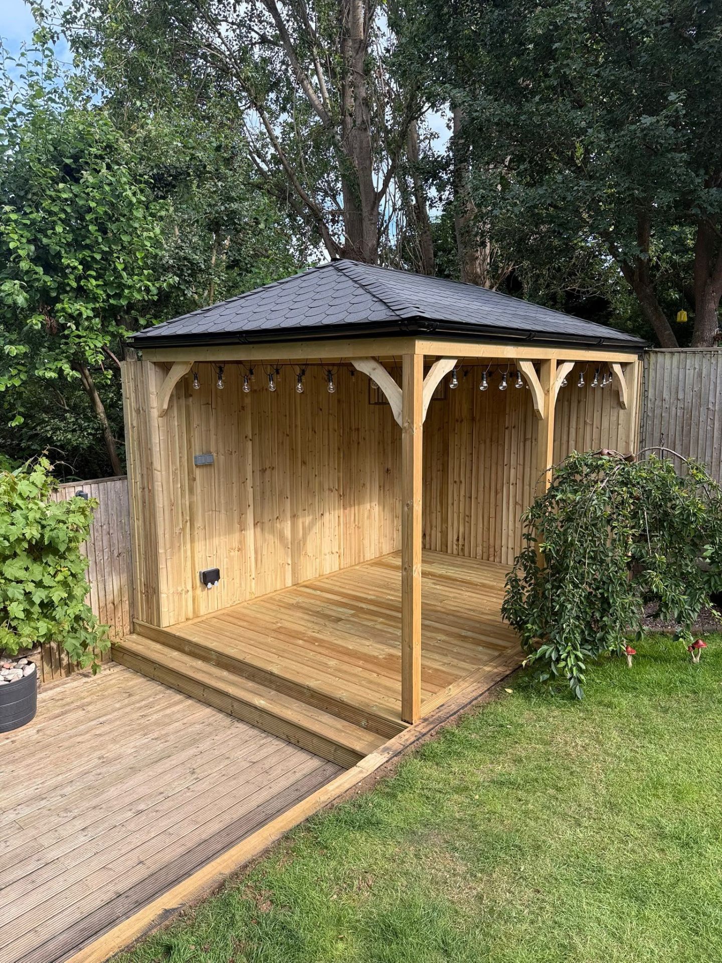 Timber garden gazebo with pitched shingle roof and festoon lighting