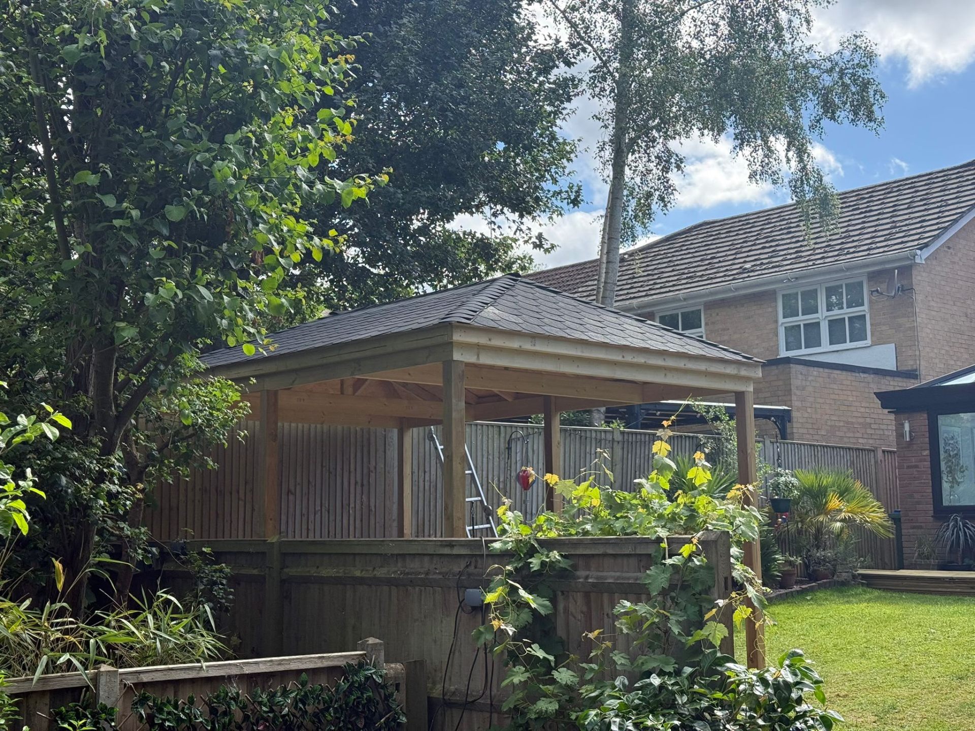 Pitched-roof garden shelter with slate tiles set among mature trees