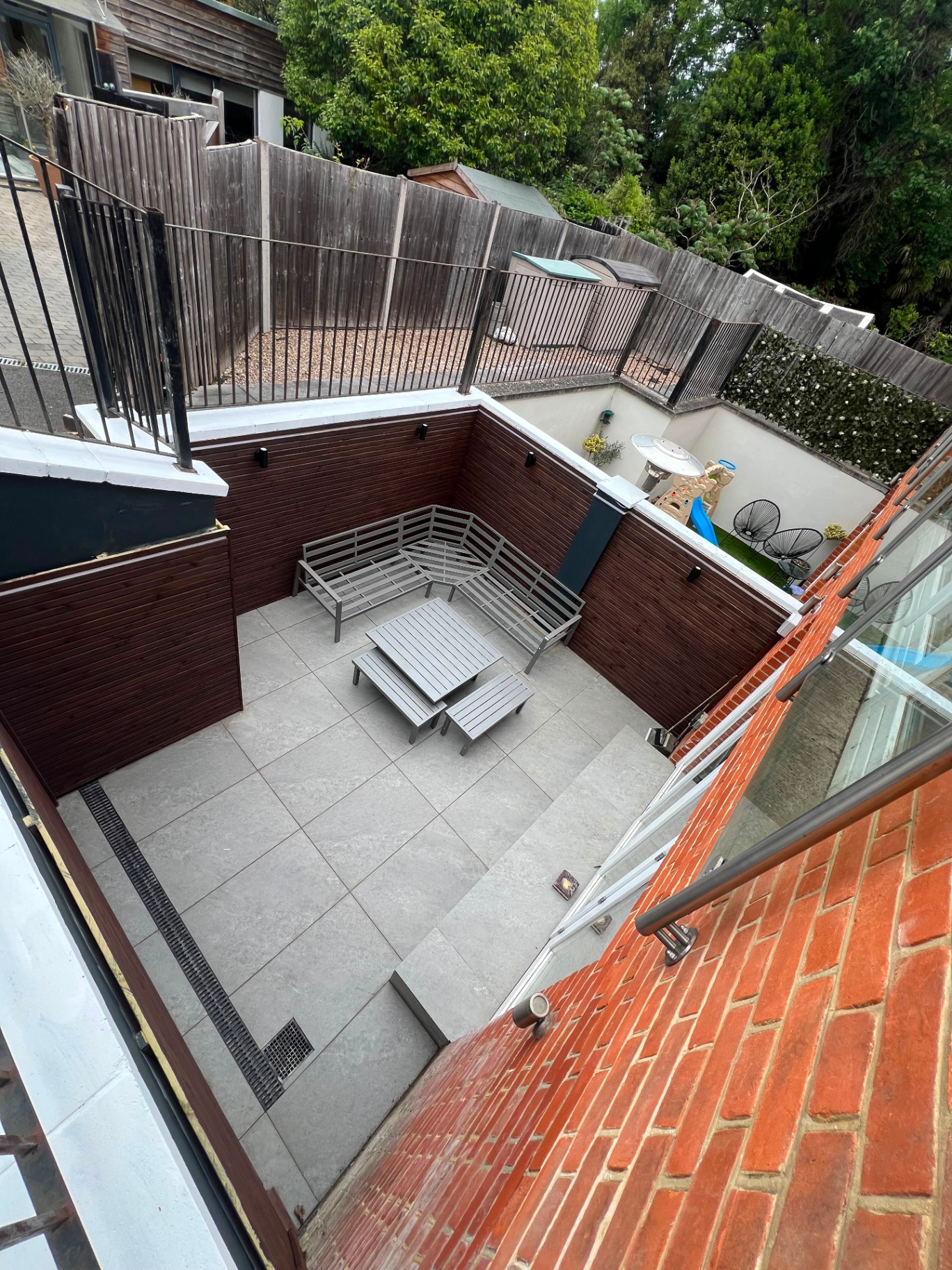 Sunken patio with porcelain paving, timber cladding and glass balustrade